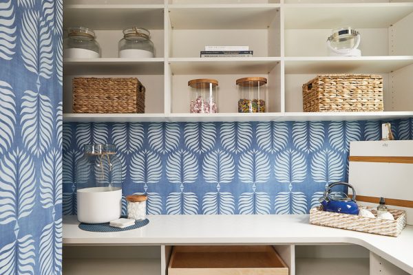 Bold wallpaper livens up this walk-in pantry and highlights the light and bright quartz countertop & white shelving.