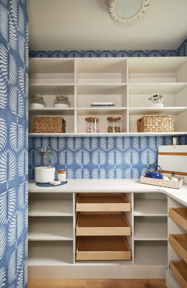 Bold wallpaper livens up this walk-in pantry and highlights the light and bright quartz countertop & white shelving.