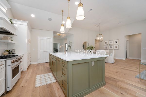 Covington Model view of the Gourmet Kitchen & Dining Room. Three gold pendants hang above an Olive Expanded Island with Quartz Countertops.