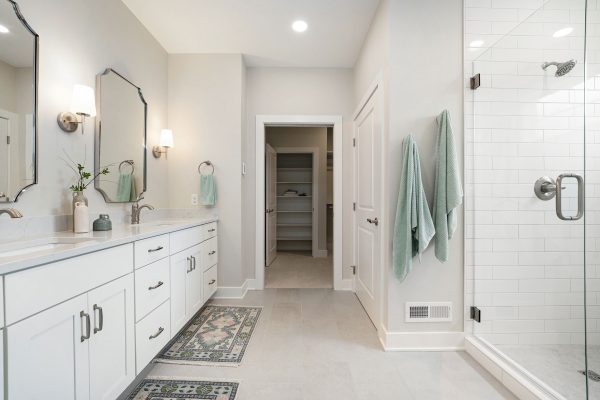 Primary Bath. To the left, there is a double vanity with warm white cabinet doors and brushed nickel hardware. To the right there is a walk-in shower with a glass enclosure & built-in bench along the widest wall. Next to the shower there a closed door to the toilet room. If you walk into the doorway directly through the bath, your spacious walk-in closet includes several types of shelving for tall and short hang as well as a linen closet.