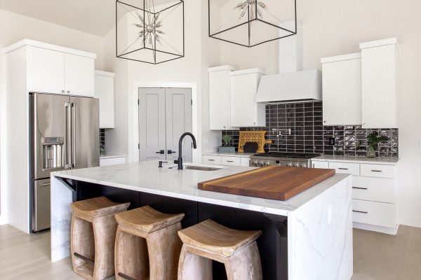 White Cabinetry grounded by expansive black island with quartz waterfall edge. Wood charcuterie display & counter-height bar stools bring warmth into the space.
