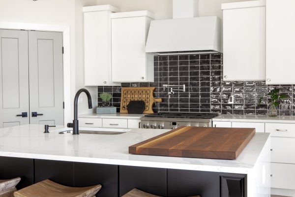 White Cabinetry grounded by expansive black island with quartz waterfall edge. Wood charcuterie display & counter-height bar stools bring warmth into the space.